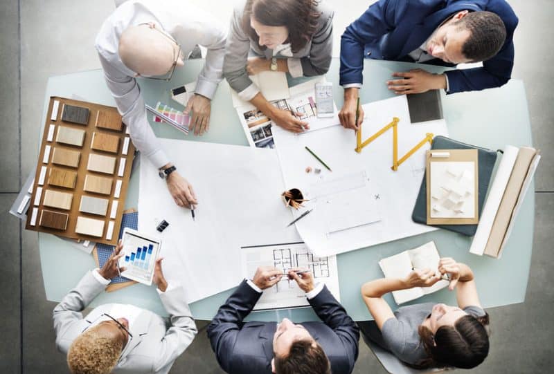 Vue de haut en bas de six professionnels collaborant autour d'une table avec des plans architecturaux et des échantillons de couleurs.