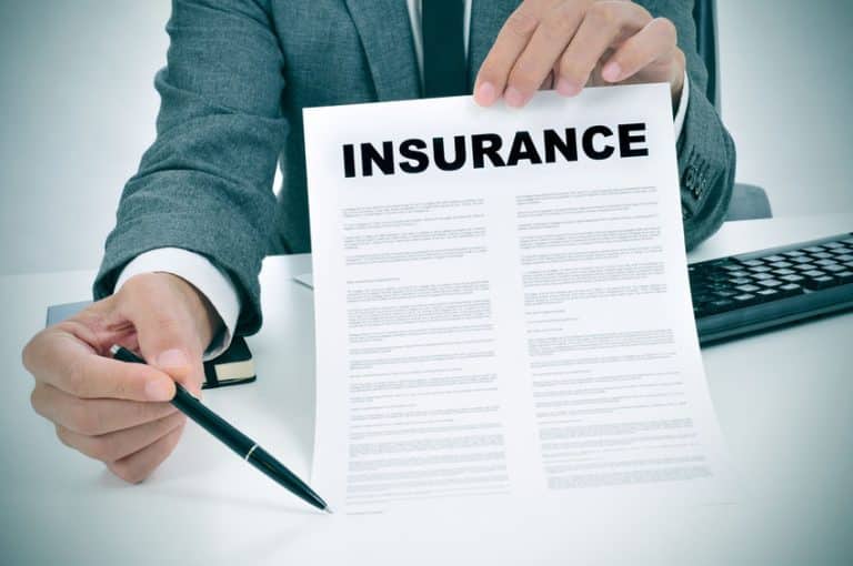 Une personne en costume présente un stylo et un document d'assurance sur un bureau, suggérant que le document est prêt à être signé.