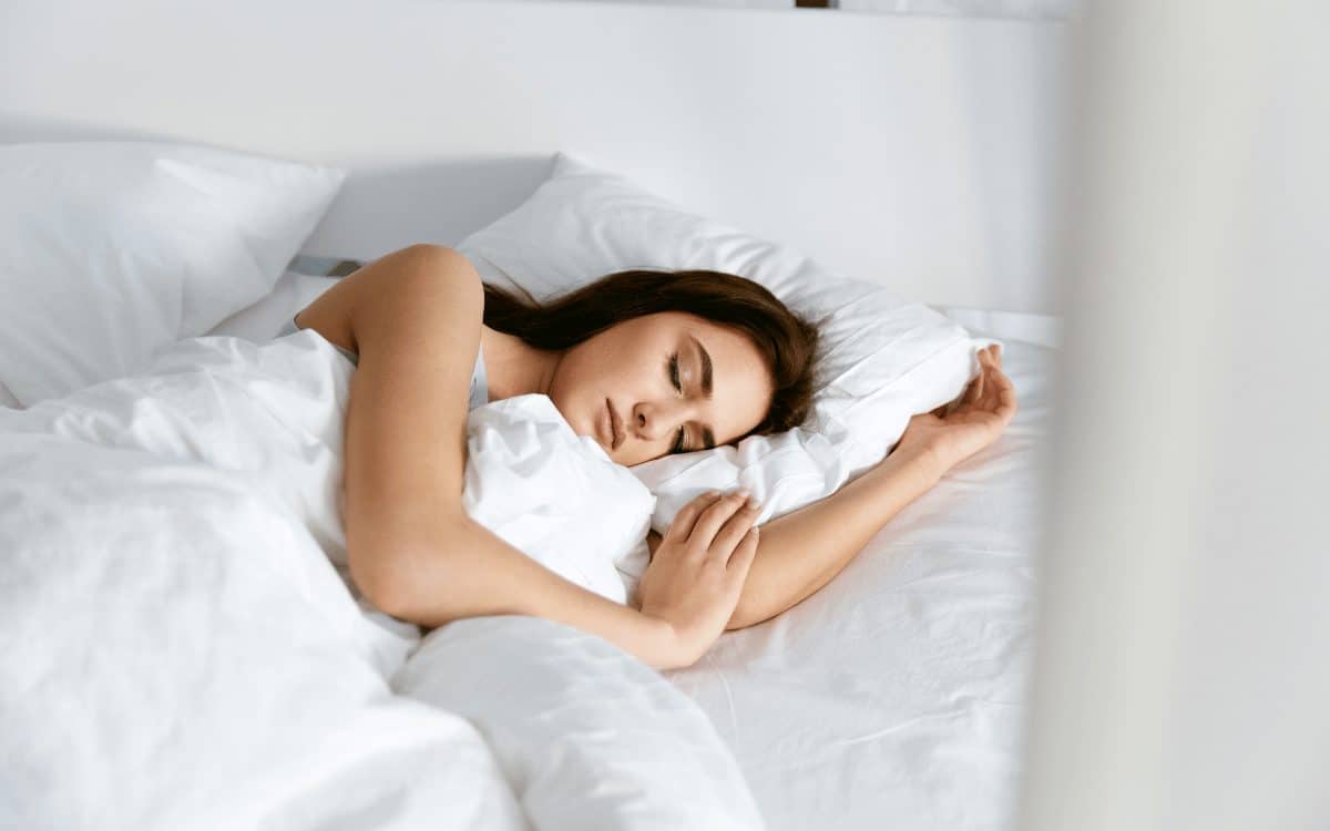 Une femme dort dans un lit avec des draps blancs.