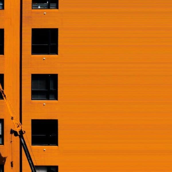 Un ouvrier dans un ascenseur inspecte ou répare la façade orange d'un bâtiment doté de plusieurs fenêtres régulièrement espacées.