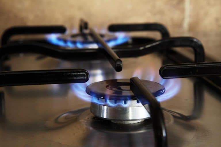 Vue rapprochée d'un brûleur de cuisinière à gaz avec une flamme bleue allumée, montrant une partie des grilles de la cuisinière et la surface en acier inoxydable.