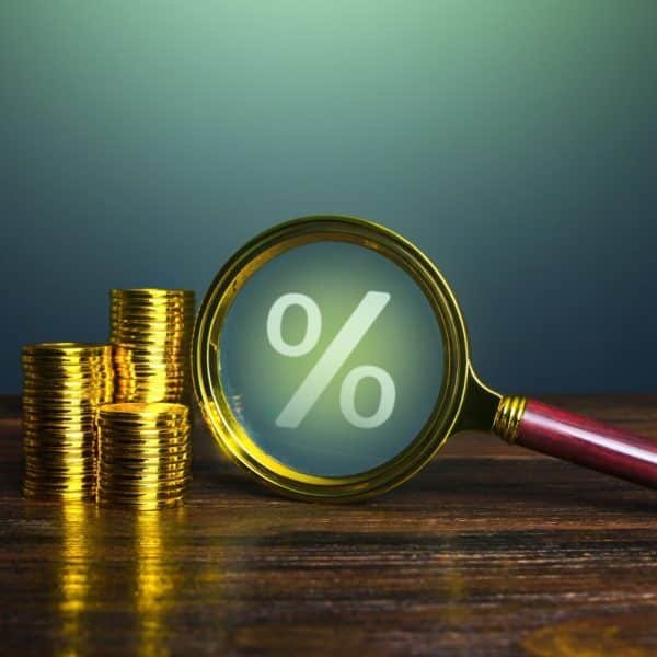 Une pile de pièces d'or à côté d'une loupe se concentrant sur un grand symbole de pourcentage sur une surface en bois.