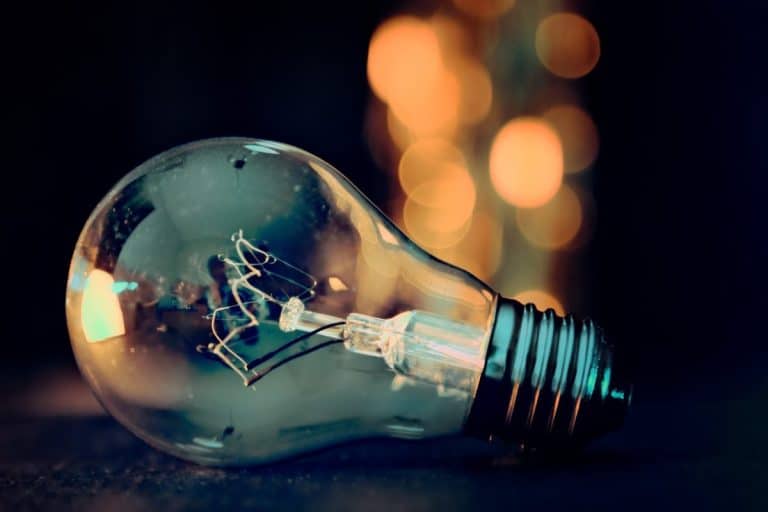 Gros plan d'une ampoule à incandescence transparente posée sur le côté sur une surface sombre, avec des lumières chaudes floues en arrière plan.