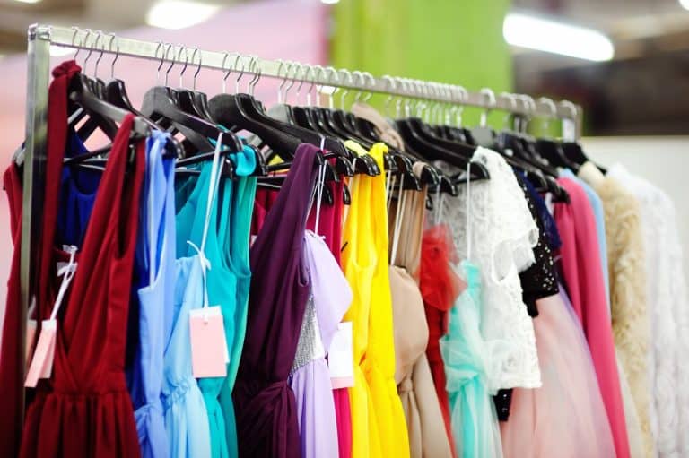 Un portant à vêtements avec différentes robes colorées, notamment rouges, bleues, jaunes et roses, chacune sur des cintres avec des étiquettes.