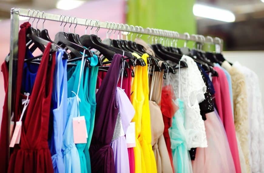 Un portant à vêtements avec différentes robes colorées, notamment rouges, bleues, jaunes et roses, chacune sur des cintres avec des étiquettes.