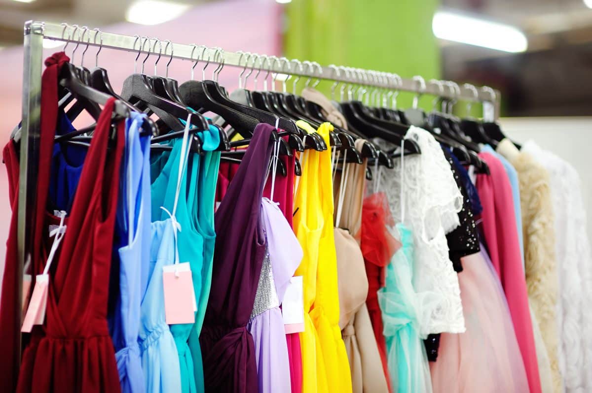 Un portant à vêtements avec différentes robes colorées, notamment rouges, bleues, jaunes et roses, chacune sur des cintres avec des étiquettes.