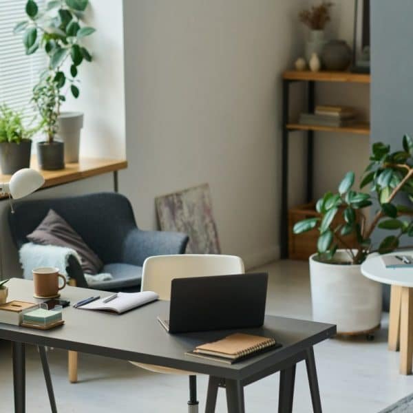 Un bureau à domicile moderne avec un ordinateur portable sur un bureau, une chaise, diverses plantes, une petite table d'appoint et des étagères en arrière plan.