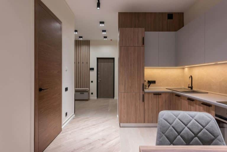 Cuisine moderne avec armoires en bois, comptoir gris et robinet noir. Le couloir adjacent est doté d'une porte en bois et de lambris muraux.