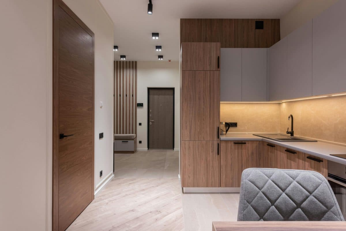 Cuisine moderne avec armoires en bois, comptoir gris et robinet noir. Le couloir adjacent est doté d'une porte en bois et de lambris muraux.