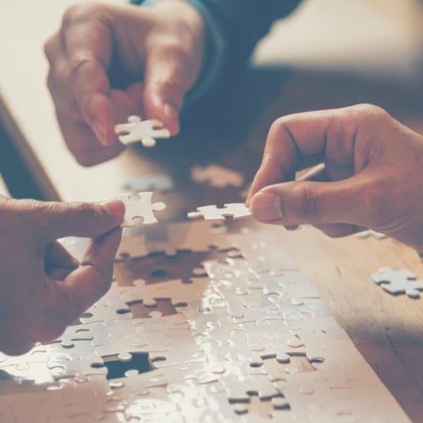Deux mains travaillent à l'assemblage d'un puzzle sur une table en bois.