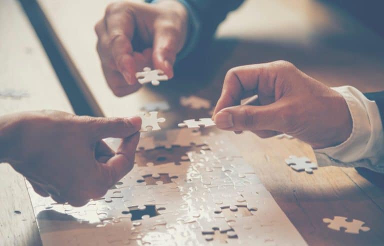 Deux mains travaillent à l'assemblage d'un puzzle sur une table en bois.