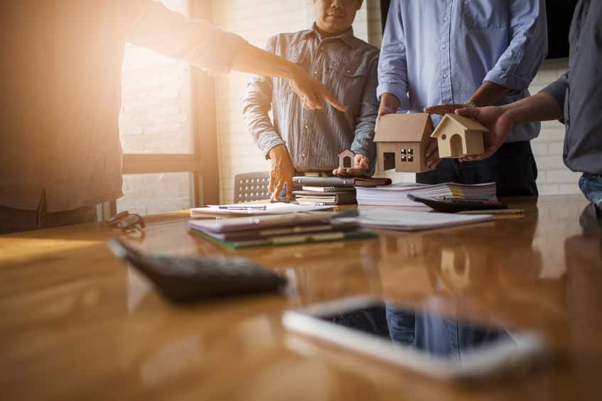 Un groupe de personnes debout autour d’une table et discutant de l’achat d’une maison.