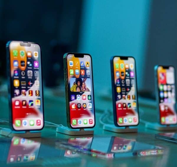 Quatre smartphones sont exposés sur des supports, chacun avec diverses icônes d'application sur leur écran, dans une pièce bien éclairée.