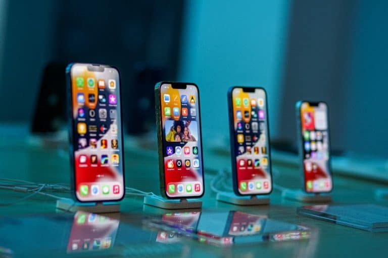 Quatre smartphones sont exposés sur des supports, chacun avec diverses icônes d'application sur leur écran, dans une pièce bien éclairée.