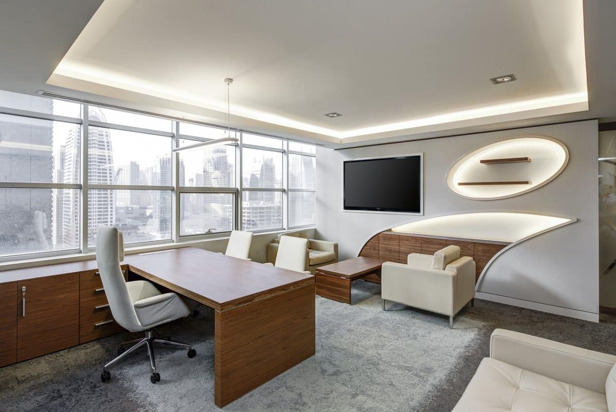 Bureau moderne avec un bureau en bois, des chaises blanches, une télévision murale et de grandes fenêtres présentant l'horizon de la ville.