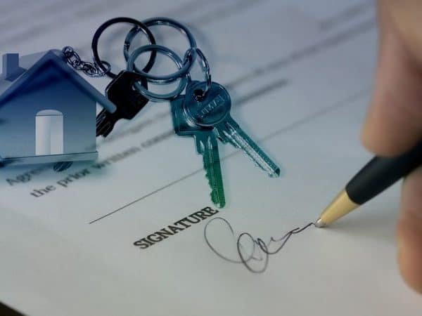 Une personne signant un document avec une maison et des clés.