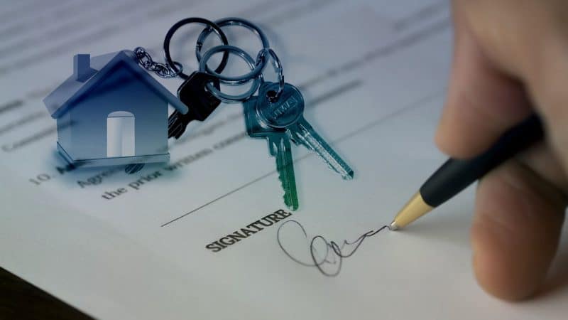 Une personne signant un document avec une maison et des clés.