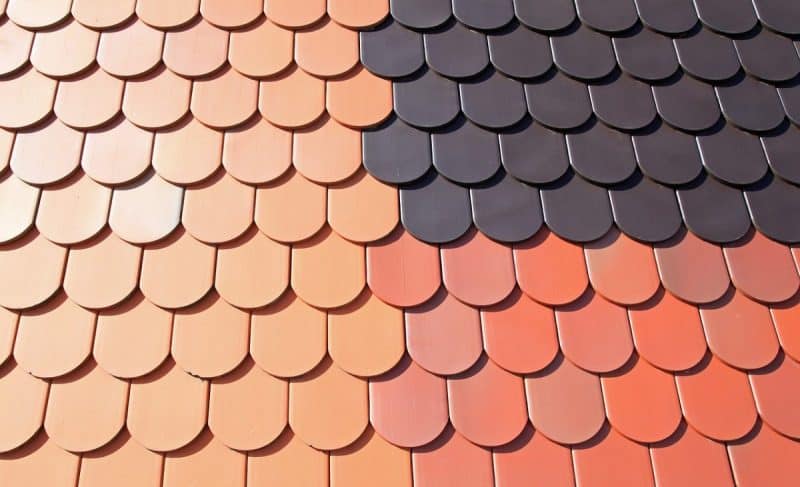 Un toit recouvert de bardeaux en écailles de poisson superposés dans diverses nuances d'orange et de noir, disposés selon un motif dégradé.