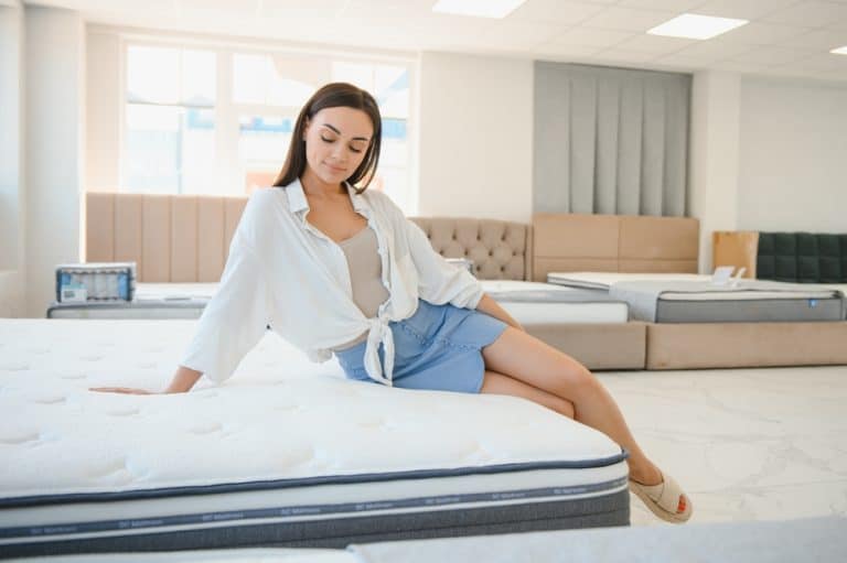 Une femme s'assoit sur le bord d'un matelas exposé dans une salle d'exposition de matelas lumineuse, pour en tester le confort.