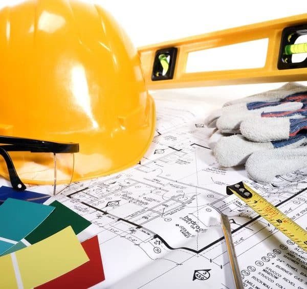 Casque de sécurité jaune, lunettes de sécurité, niveau, ruban à mesurer, gants, échantillons de couleurs et plans architecturaux disposés sur une table.