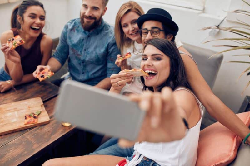 Un groupe d'amis prenant un selfie en mangeant une pizza.
