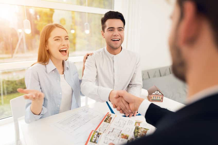 Un homme et une femme se serrent la main à une table tout en regardant un plan de maison.