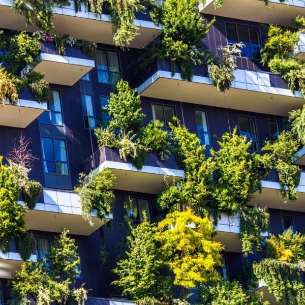 Un immeuble d'appartements moderne avec des balcons couverts de plantes et d'arbres verts luxuriants, créant une façade de jardin verticale.