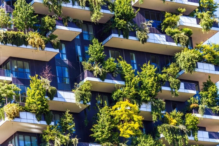 Un immeuble d'appartements moderne avec des balcons couverts de plantes et d'arbres verts luxuriants, créant une façade de jardin verticale.