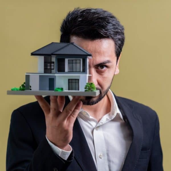 Un homme tenant une maquette de maison devant son visage.