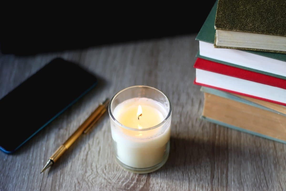 Une bougie est posée au dessus d’une pile de livres et d’un téléphone.