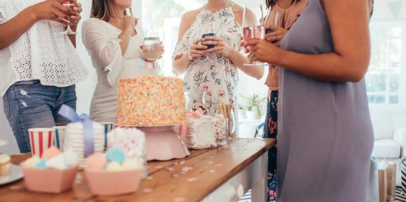 Un groupe de femmes debout autour d’une table avec des gâteaux et des boissons.