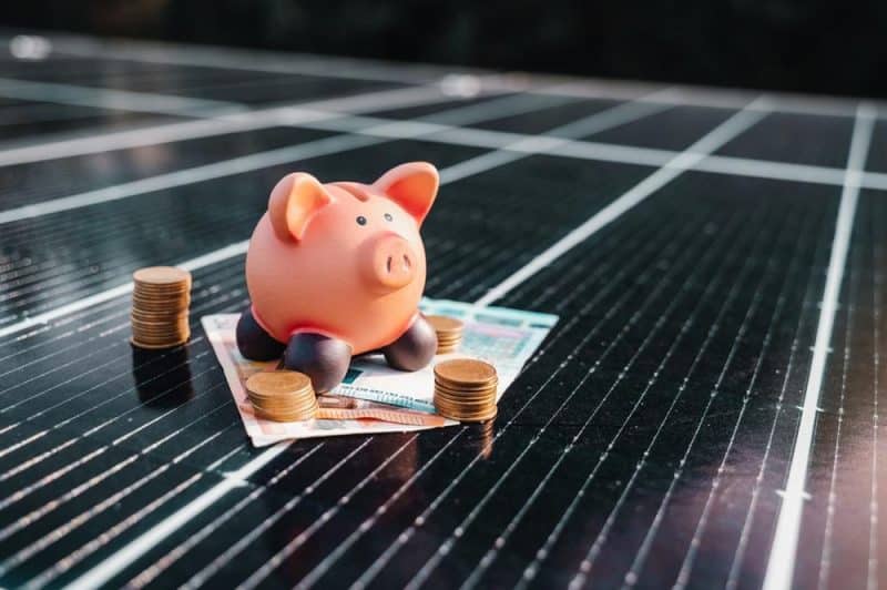 Tirelire et pièces de monnaie sur des billets de banque posés sur un panneau solaire.
