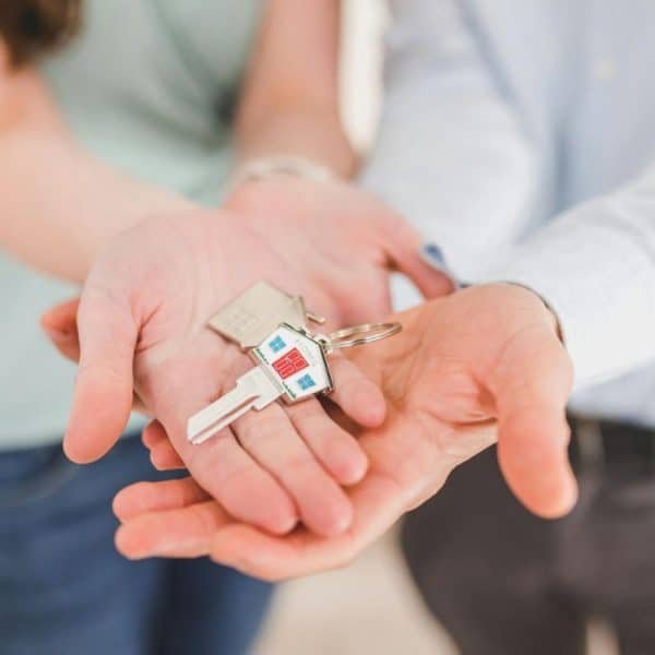Deux personnes tendent ensemble un trousseau de clés de maison, avec un petit porte clés en forme de maison visible dans leurs mains ouvertes.