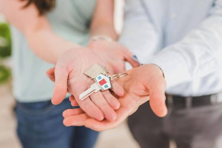 Deux personnes tendent ensemble un trousseau de clés de maison, avec un petit porte clés en forme de maison visible dans leurs mains ouvertes.