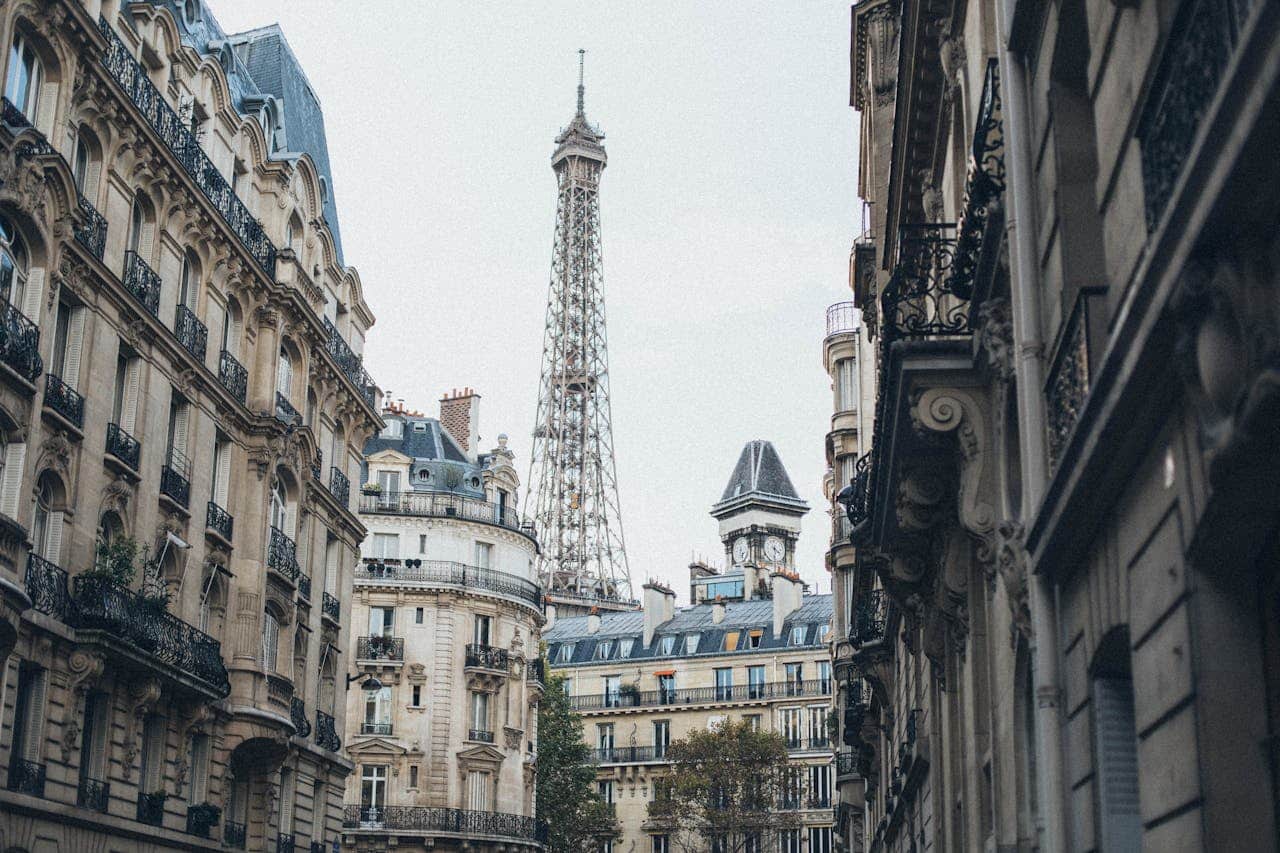Vue de la Tour Eiffel encadrée par des bâtiments parisiens historiques sous un ciel nuageux.