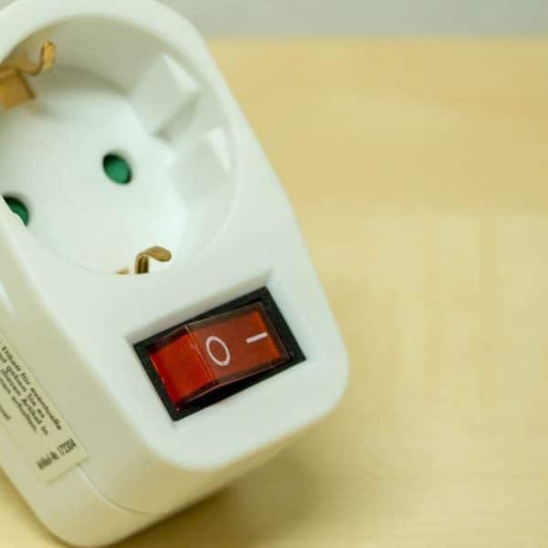 Un adaptateur de prise électrique blanc avec un interrupteur marche/arrêt rouge est placé sur une surface en bois.