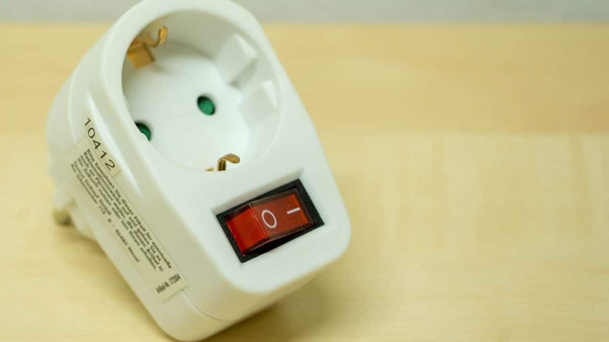 Un adaptateur de prise électrique blanc avec un interrupteur marche/arrêt rouge est placé sur une surface en bois.