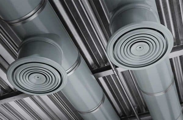 Deux conduits d'air cylindriques en métal fixés à un plafond avec des bouches d'aération circulaires orientées vers le bas, sur fond de panneaux de plafond en métal.