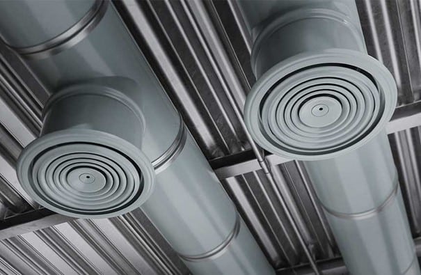 Deux conduits d'air cylindriques en métal fixés à un plafond avec des bouches d'aération circulaires orientées vers le bas, sur fond de panneaux de plafond en métal.