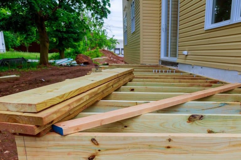Terrasse en bois en construction avec des planches empilées près d'une maison.