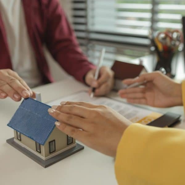 A man signs a contract after agreeing to buy a house with an agent. The agent explains the details o