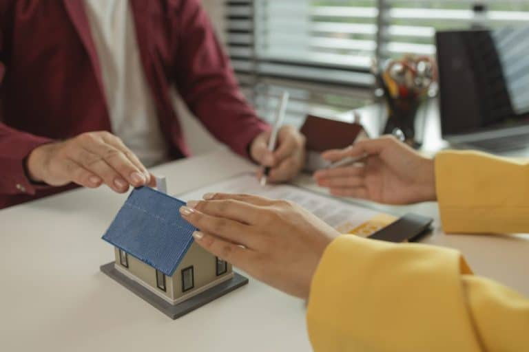 A man signs a contract after agreeing to buy a house with an agent. The agent explains the details o