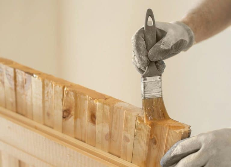 Une main gantée applique du vernis avec un pinceau sur une porte en bois.