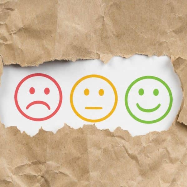 Trois émoticônes sur du papier déchiré : un visage triste rouge, un visage neutre jaune et un visage heureux vert.