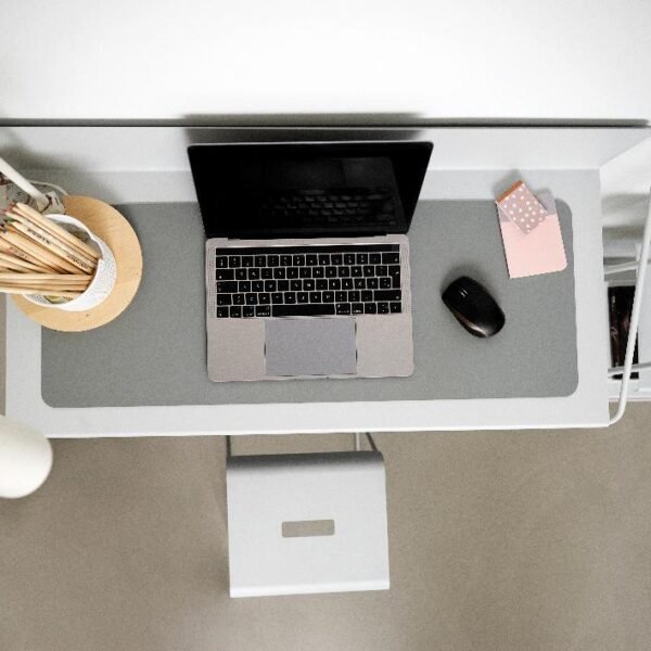 Vue d'ensemble d'un bureau minimaliste avec un ordinateur portable, une lampe, un pot de crayons, une souris et deux petits blocs-notes sur un tapis de bureau gris.