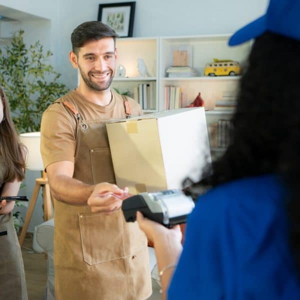 Un homme en tablier paie un livreur avec une carte de crédit tandis qu'une femme en tablier prend des notes à l'arrière plan.