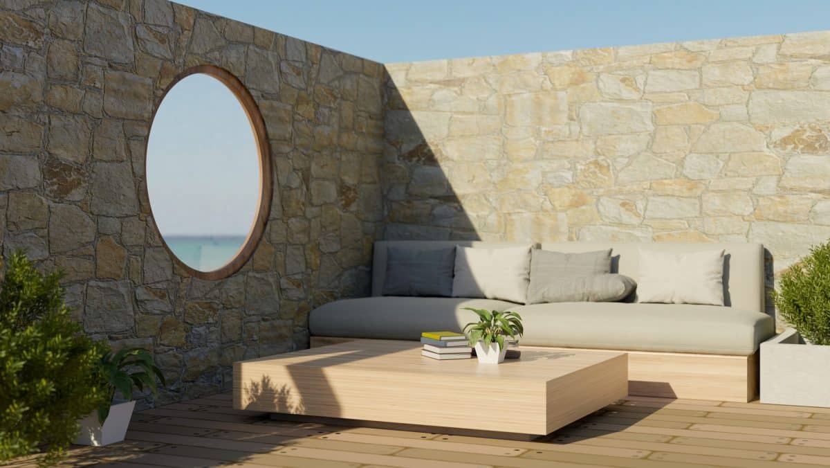 Beautiful outdoor terrace design with comfortable couch, circle window with beach view, stone wall.
