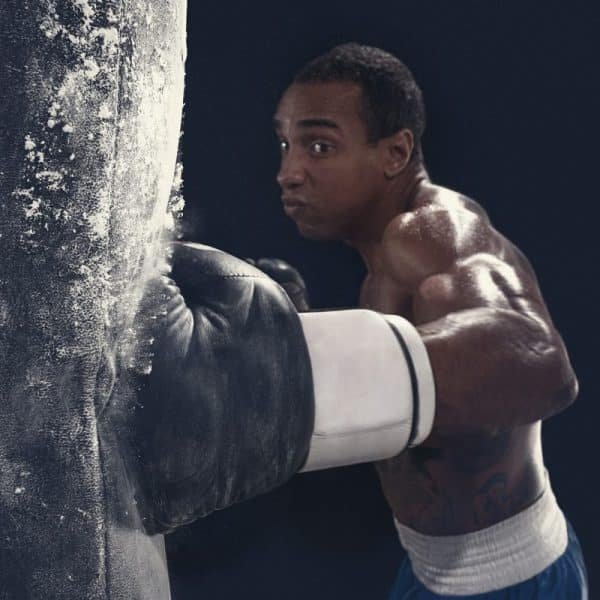 Un boxeur portant des gants blancs et un short bleu frappe un sac de frappe avec concentration et force.