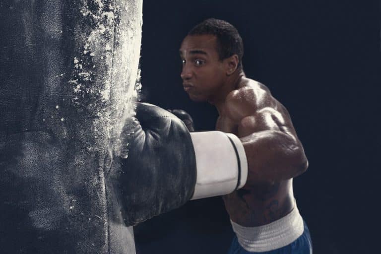Un boxeur portant des gants blancs et un short bleu frappe un sac de frappe avec concentration et force.