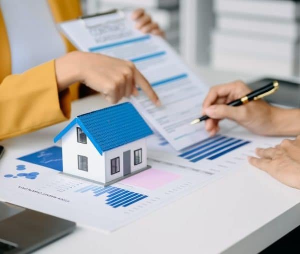 Deux professionnels discutent de documents avec une petite maison modèle sur la table, indiquant une réunion de planification immobilière ou financière.